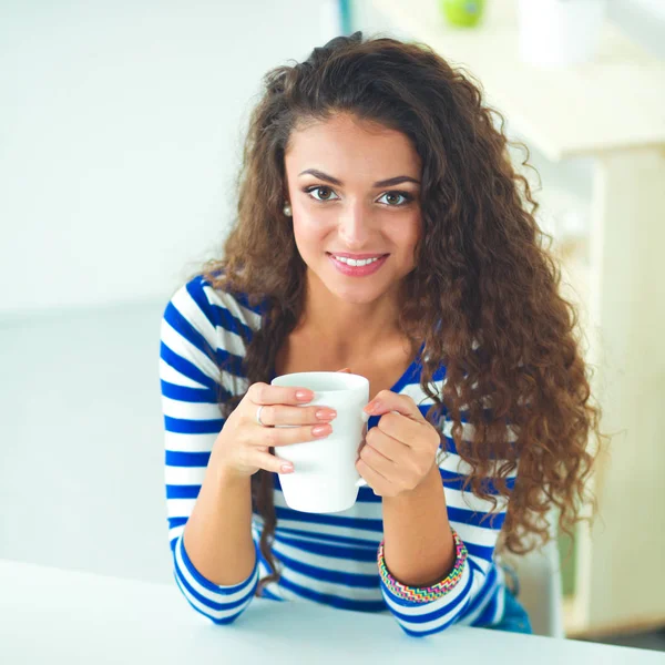 Sorrindo jovem com xícara de café e laptop na cozinha em casa — Fotografia de Stock