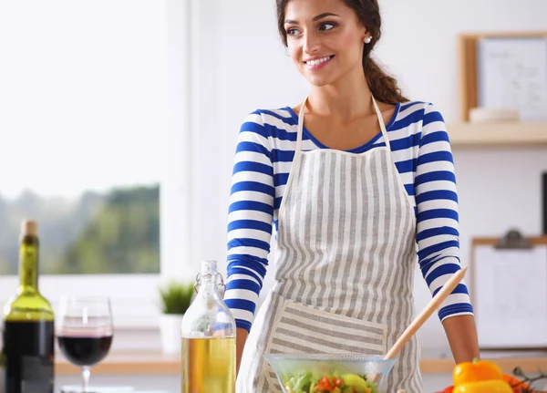 Sorrindo jovem mulher misturando salada fresca, de pé perto da mesa — Fotografia de Stock