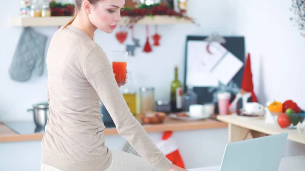 Nő használ egy laptop, miközben ivás lé a konyhában — Stock Fotó