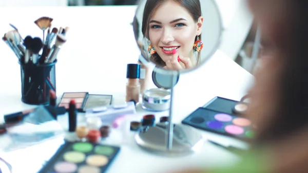 Jeune belle femme se maquillant près du miroir, assise au bureau — Photo