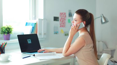 Genç iş kadını masada oturuyor ve telefonla konuşuyor.