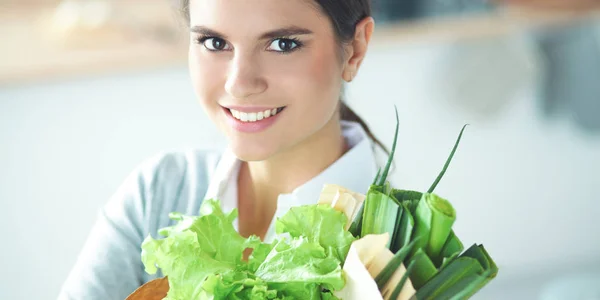 Mujer joven sosteniendo bolsa de la compra de comestibles con verduras de pie en la cocina. —  Fotos de Stock