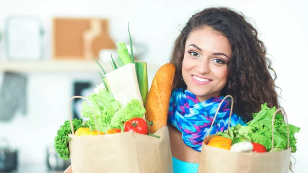 Mujer joven sosteniendo bolsa de la compra de comestibles con verduras de pie en la cocina. — Foto de Stock