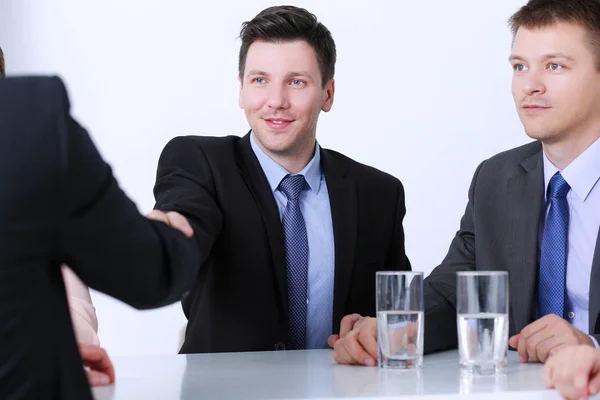 Compañeros de negocios sentados en una mesa durante una reunión con dos hombres dándose la mano —  Fotos de Stock