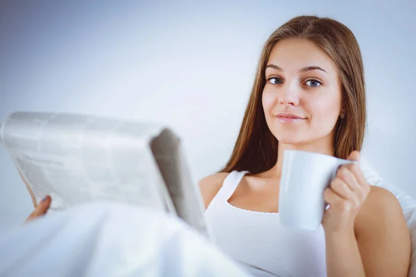 かなり若い女性ベッドで新聞を読むと、紅茶のカップを楽しむ — ストック写真