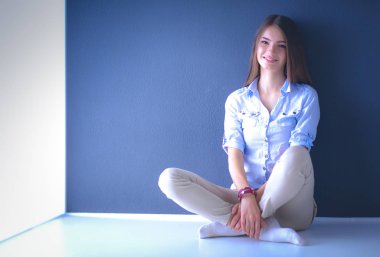 Genç bir kadın yerde, kara duvarın yanında oturuyor.