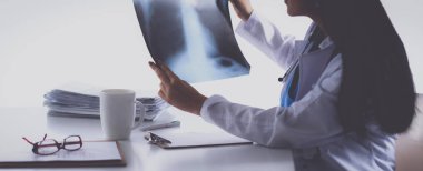 Genç bayan doktor röntgen üzerinde çalışıyor, masada oturuyor.