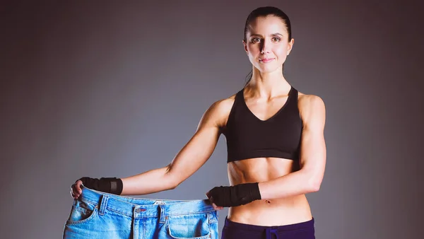 Giovane donna fitness che mostra che i suoi vecchi jeans — Foto Stock