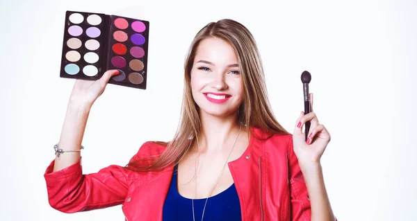 Mladá krásná žena drží v jedné ruce a paletu s barvou a stíny na make-up, druhý ruční štětec na make-up — Stock fotografie