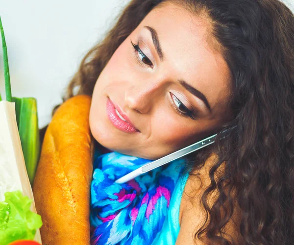 Glimlachende vrouw met mobiele telefoon houden boodschappentas in de keuken — Stockfoto