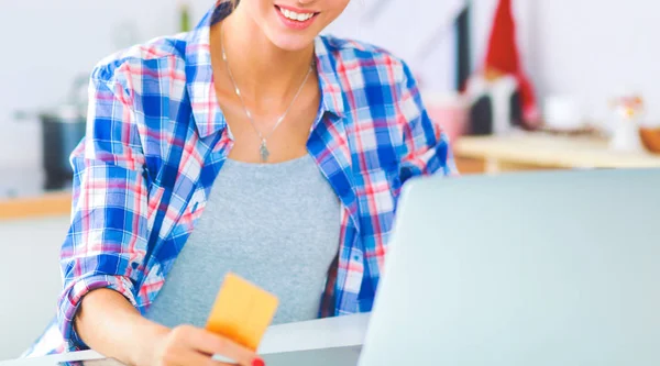 Mujer sonriente compras en línea utilizando la computadora y la tarjeta de crédito en la cocina — Foto de Stock