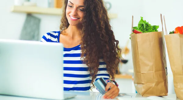 Lachende vrouw online winkelen met behulp van computer en creditcard in de keuken — Stockfoto