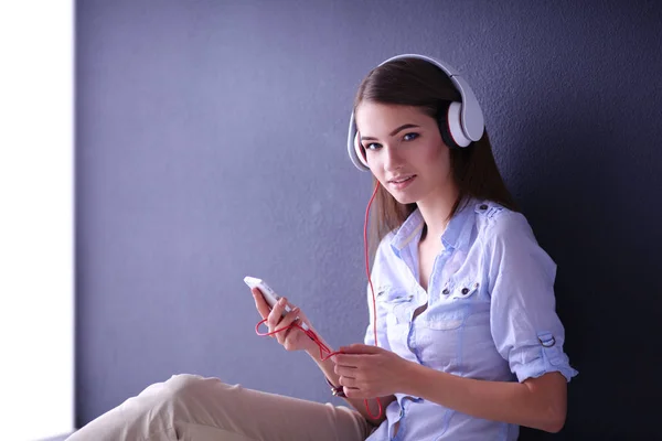 Chica sonriente con auriculares sentados en el suelo cerca de la pared —  Fotos de Stock