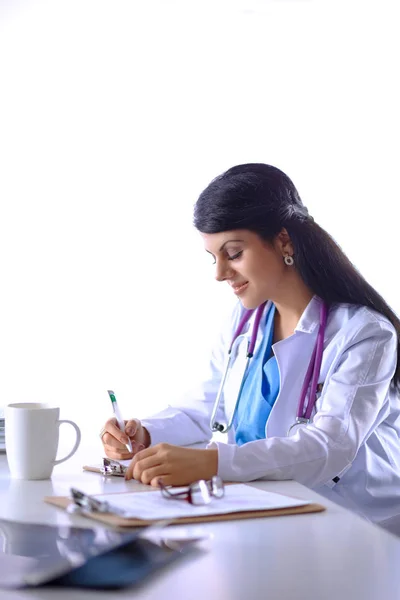 Bonito jovem sorridente médico feminino sentado na mesa — Fotografia de Stock