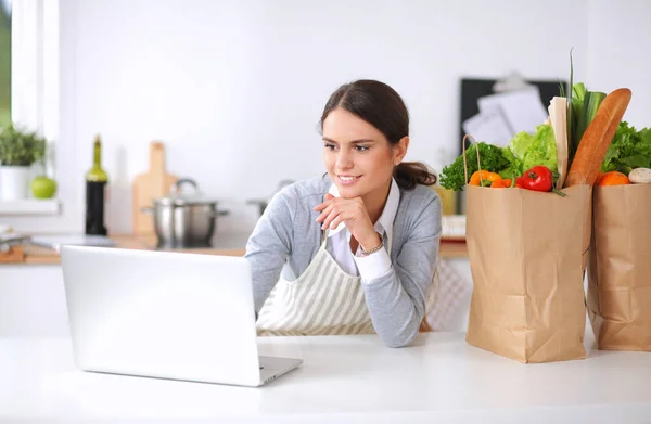 Mujer sonriente compras en línea utilizando la computadora y la tarjeta de crédito en la cocina —  Fotos de Stock