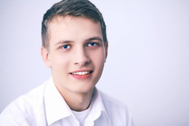 Gri arka plan üzerinde oturan gülümseyen genç adam portresi