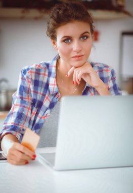 Mutfakta bilgisayar ve kredi kartı kullanan gülümseyen bir kadın.