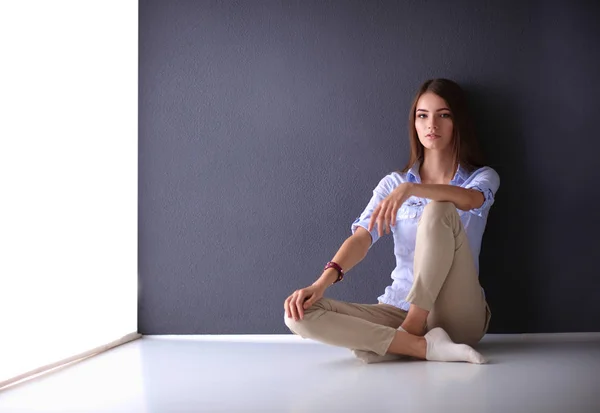 Giovane donna seduta sul pavimento vicino al muro scuro — Foto Stock