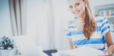 Elinde evrakları olan kadın masanın üstünde oturuyor.