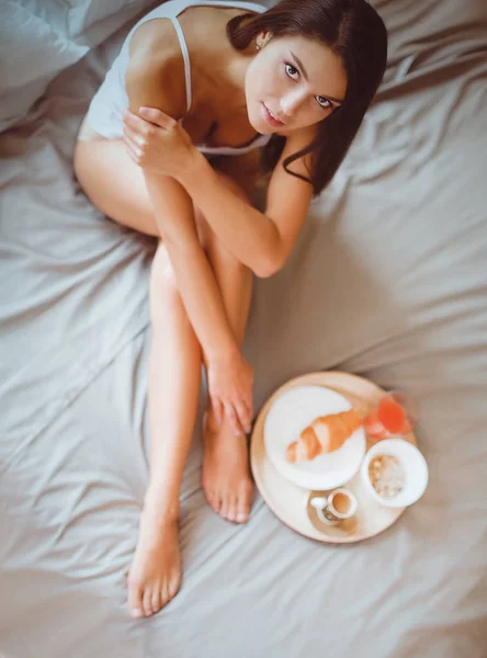 Young woman sitting in bed with a cup of milk — Stock Photo, Image