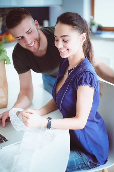 Pareja pagando sus cuentas con el ordenador portátil en la cocina en casa — Foto de Stock