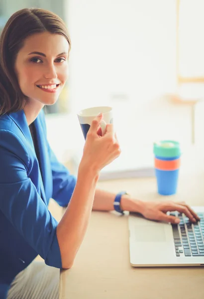 Atractiva mujer de negocios sonriente sentada en el escritorio de la oficina, sosteniendo una taza de café — Foto de Stock