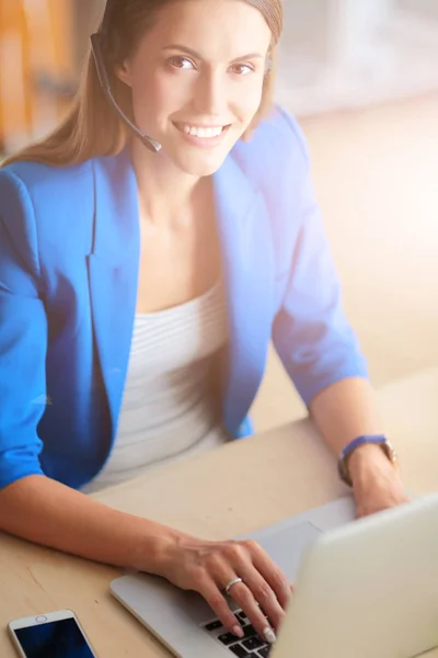 Porträtt av vacker affärskvinna som arbetar vid sitt skrivbord med headset och laptop. — Stockfoto