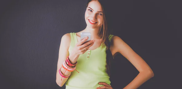 Beautiful businesswoman using cell phone standing near wall — Stock Photo, Image