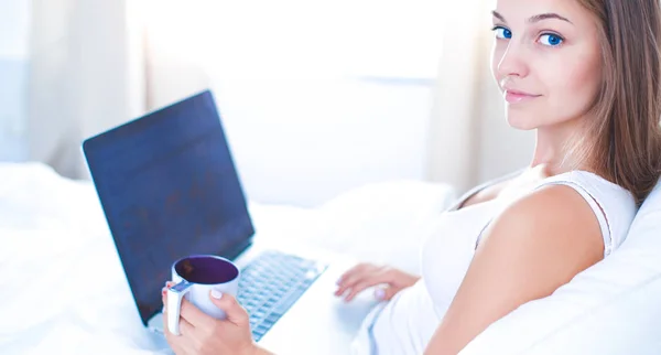 Jolie jeune femme avec ordinateur portable au lit et profiter d'une tasse de thé — Photo