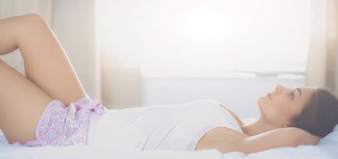 Güzel genç bir kadın, rahat ve mutlu bir şekilde yatakta uzanıyor.