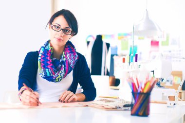 Güzel moda tasarımcısı stüdyoda masada oturuyor. .