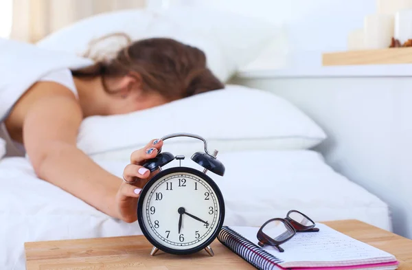 Una mujer joven apagando su despertador por la mañana. — Foto de Stock