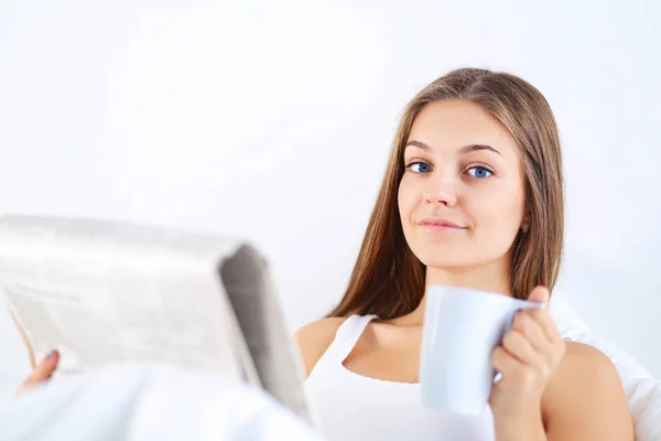 かなり若い女性ベッドで新聞を読むと、紅茶のカップを楽しむ. — ストック写真