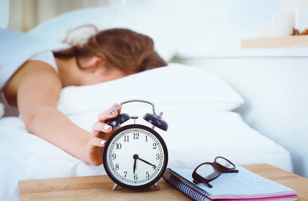 Una mujer joven apagando su despertador por la mañana. — Foto de Stock