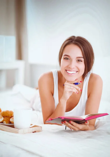Young beautiful woman sitting in bed and writing in a copybook. — Stock Photo, Image