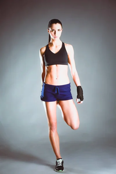 Muscular young woman posing in sportswear against black background. — Stock Photo, Image