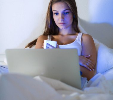 Yatak ve çay tadını çıkarırken bir dizüstü bilgisayar ile genç ve güzel bir kadın