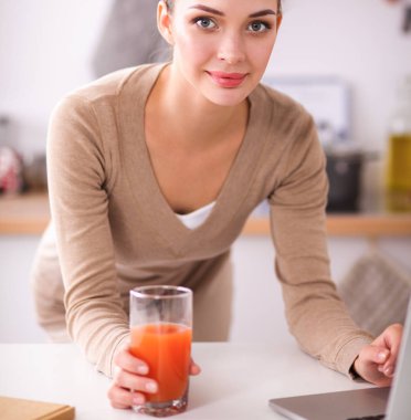 mutfağında suyu yudumlarken bir dizüstü bilgisayar kullanan kadın