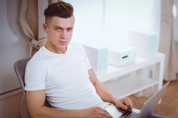 Ung man sitter på stol med laptop — Stockfoto