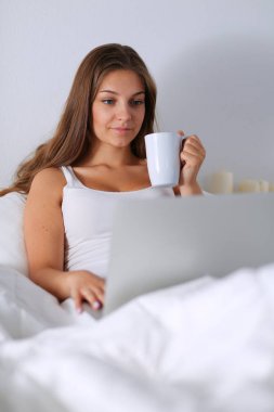 Yatak ve çay tadını çıkarırken bir dizüstü bilgisayar ile genç ve güzel bir kadın