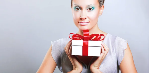 Junge Frau glücklich lächelnd Geschenkbox in den Händen halten, isoliert über grauem Hintergrund — Stockfoto