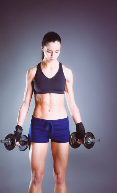 Koyu arkaplanda dambıllarla egzersiz yapan genç bir kadın..