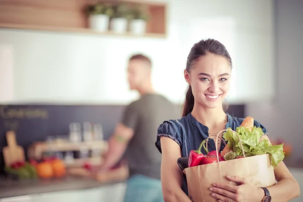 Unga par i köket, kvinna med en påse livsmedel shopping — Stockfoto