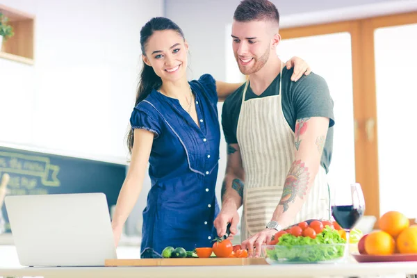 Jovem cortando legumes e mulher de pé com laptop na cozinha — Fotografia de Stock