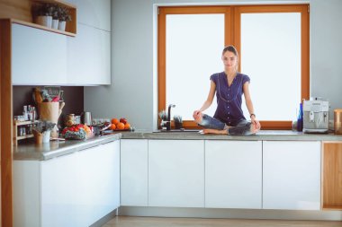 Lotus pozisyonunda mutfak masasında oturan genç güzel kadın