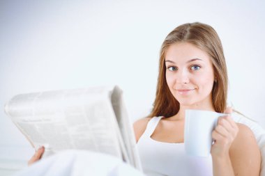 Genç ve güzel bir kadın yatakta gazete okuyan ve bir fincan çay keyfi.