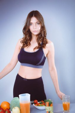 Sebzelerle masanın yanında duran genç ve güzel bir kadın..