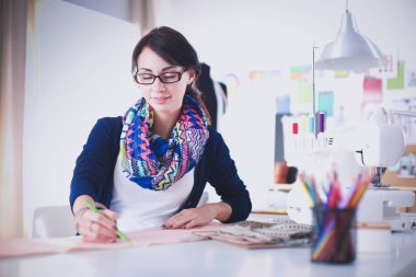 Güzel moda tasarımcısı stüdyoda masada oturuyor. .