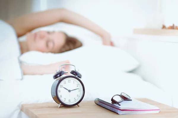 Una mujer joven apagando su despertador por la mañana. — Foto de Stock