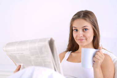 Genç ve güzel bir kadın yatakta gazete okuyan ve bir fincan çay keyfi.